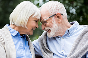 Elderly couple outside with their foreheads touching smiling at each other